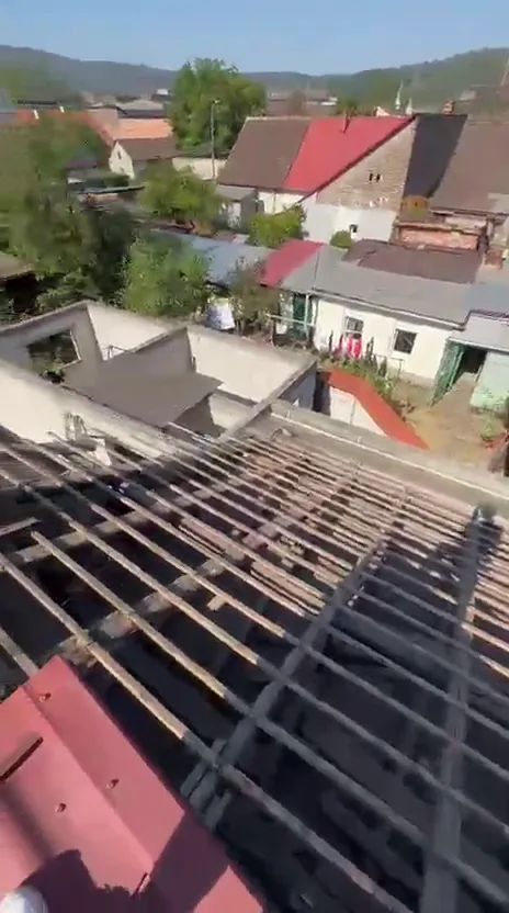Acoperiș vechi decopertat: șipca și căpriorii rămân la vedere peste sat, cu țigla veche strânsă pe margine.