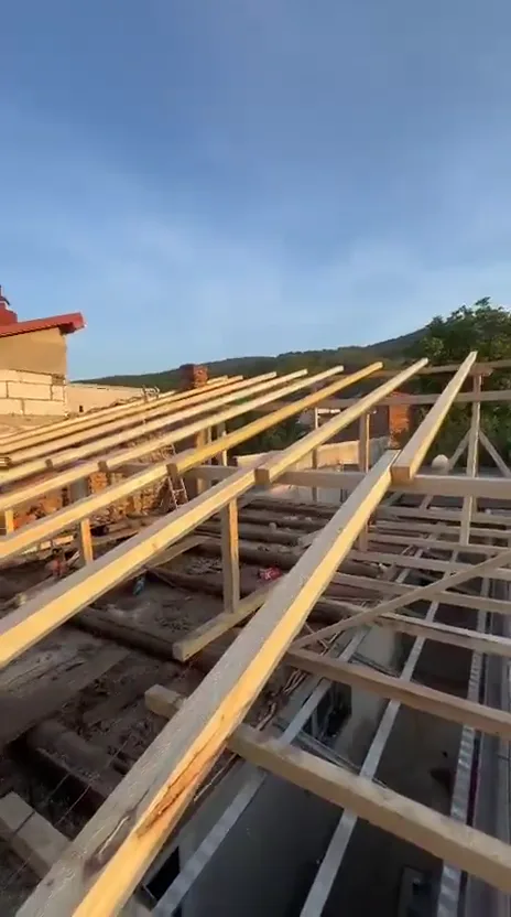 Căpriori noi de brad montați pe o casă la roșu, cu folia trasă deja pe fronton.