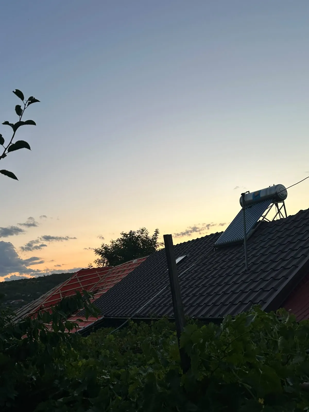 Siluetă de acoperiș cu panou solar montat pe versant, profilată pe cerul unui apus portocaliu.