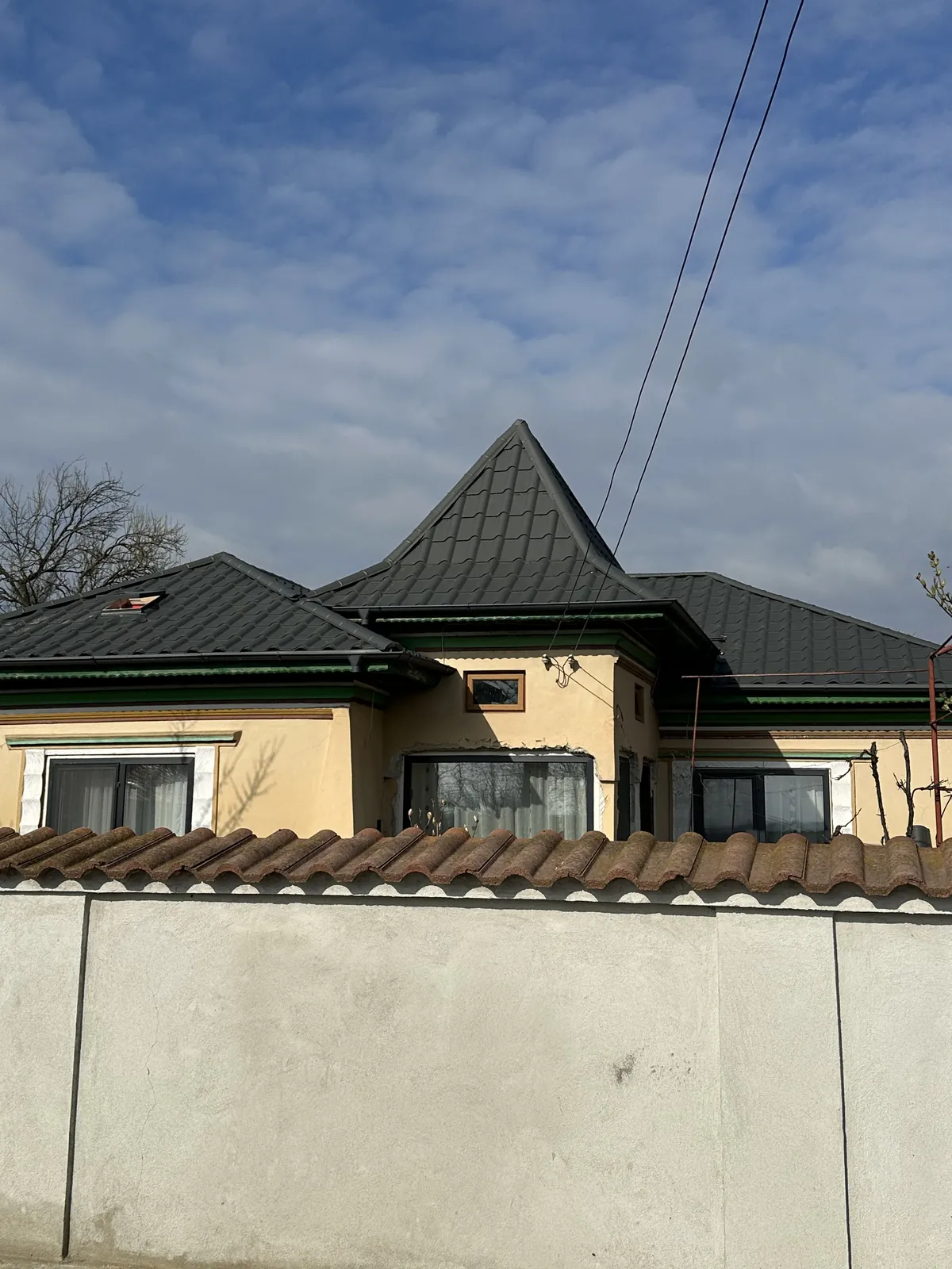 Casă cu turelă rotundă acoperită cu învelitoare tip solzi de culoare închisă, deasupra unui gard de beton.