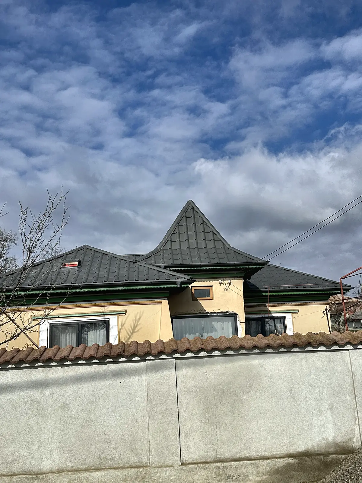 Casă cu acoperiș nou și turelă peste colț, văzută peste zidul de la stradă.