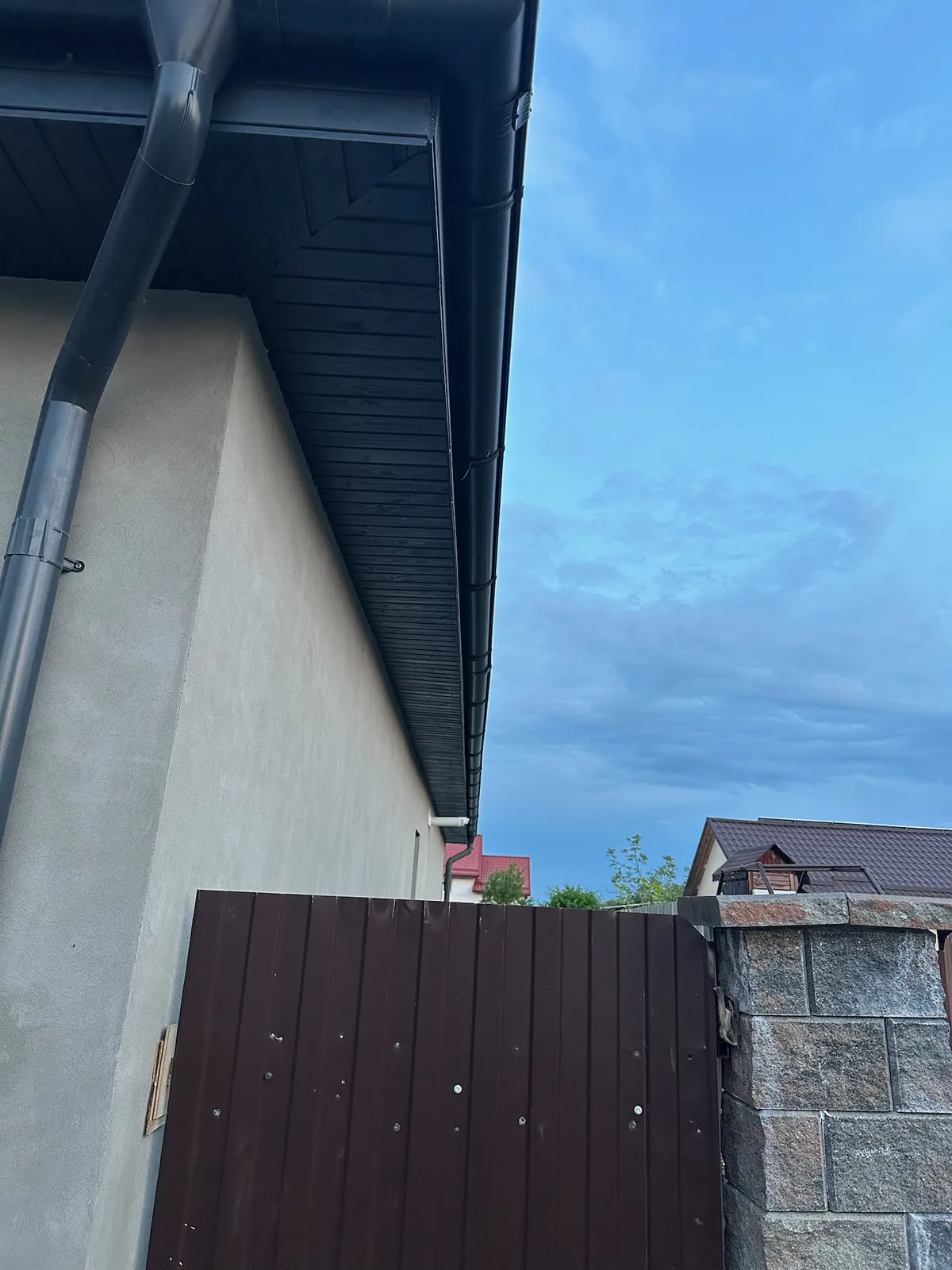 Colț de streașină nouă cu jgheab și burlan zincat proaspăt montate pe o casă tencuită.