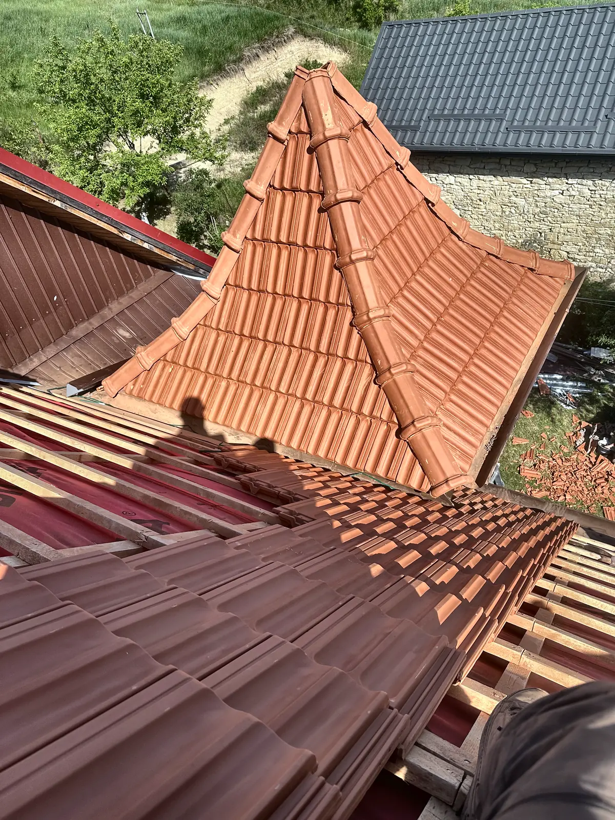 Acoperiș de țiglă ceramică roșie, cu coama și doliile în lucru.