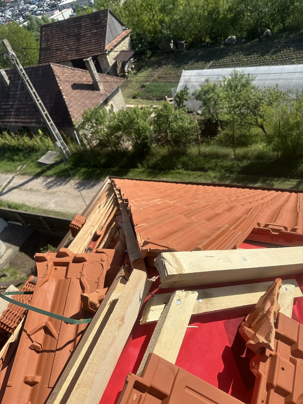 Țiglă ceramică portocalie și elemente de coamă așezate pe folia roșie a unui acoperiș în lucru.