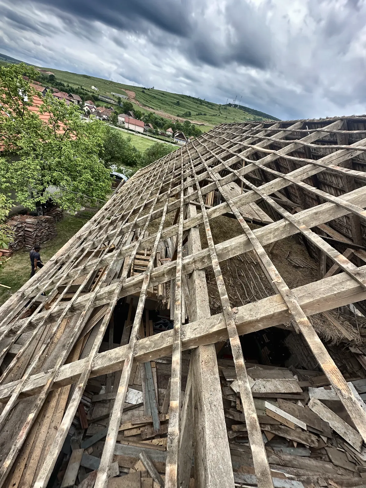 Acoperiș vechi decopertat până la șipci și căpriori, cu satul în vale.