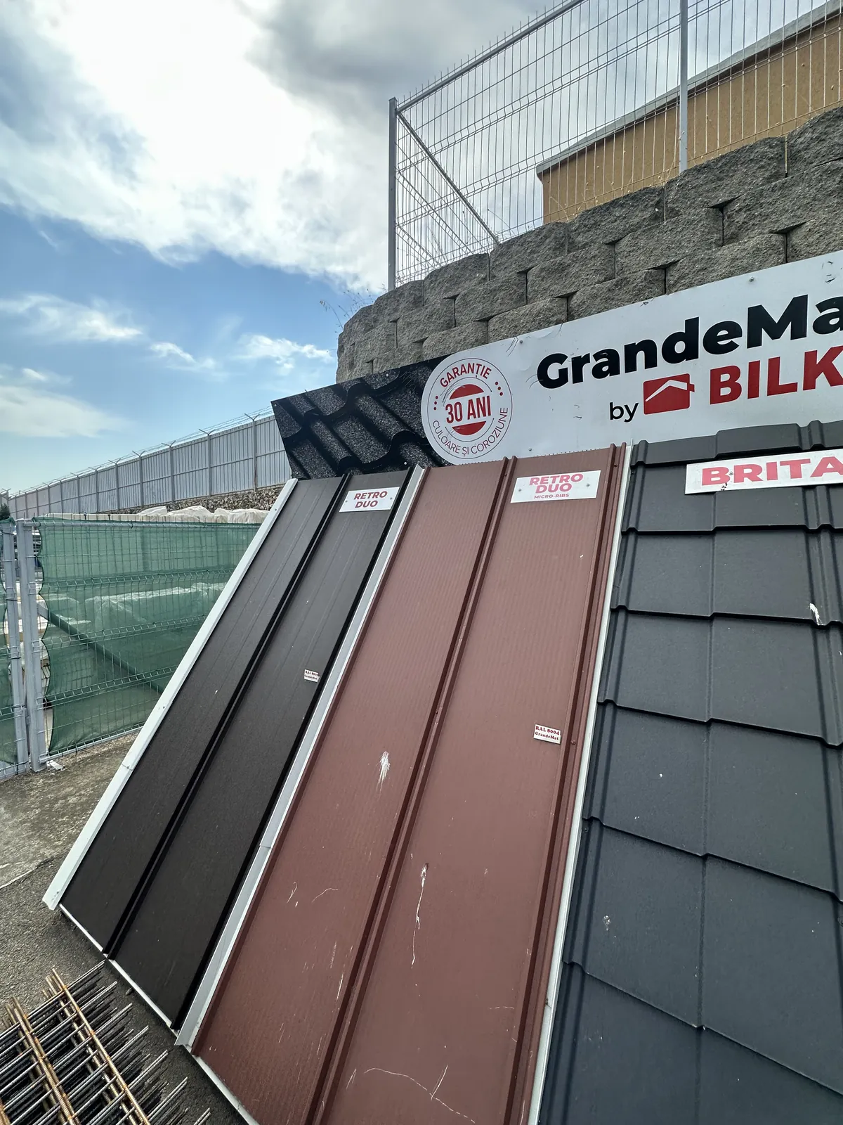 Panouri de tablă fălțuită maro și gri așezate pe un stand de prezentare, cu falțurile verticale vizibile.