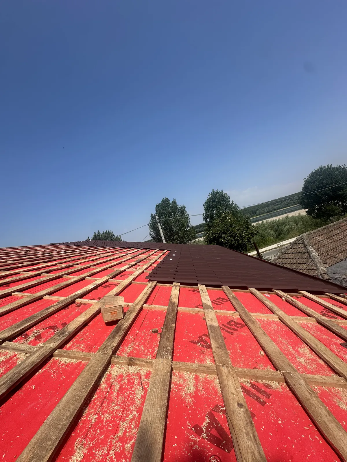 Versant decopertat cu folie roșie și șipci noi, cu rândurile de țiglă maro montate în partea de sus a acoperișului.