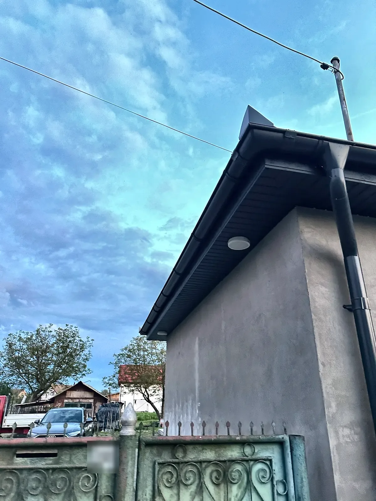 Fronton de casă cu streașina închisă și burlanul montat, văzut de la poartă.