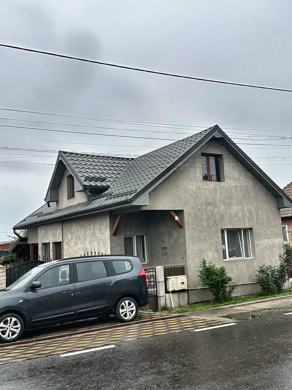 Casă cu acoperiș gri și lucarnă, văzută de peste drum.